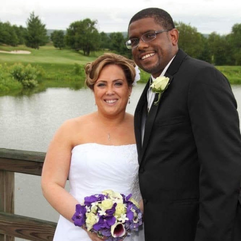 A bride and groom stand side-by-side on a bridge on a lakefront