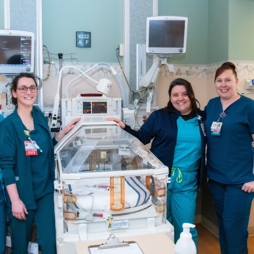 Three women neonatal nurses smiling around an incubator in the NICU