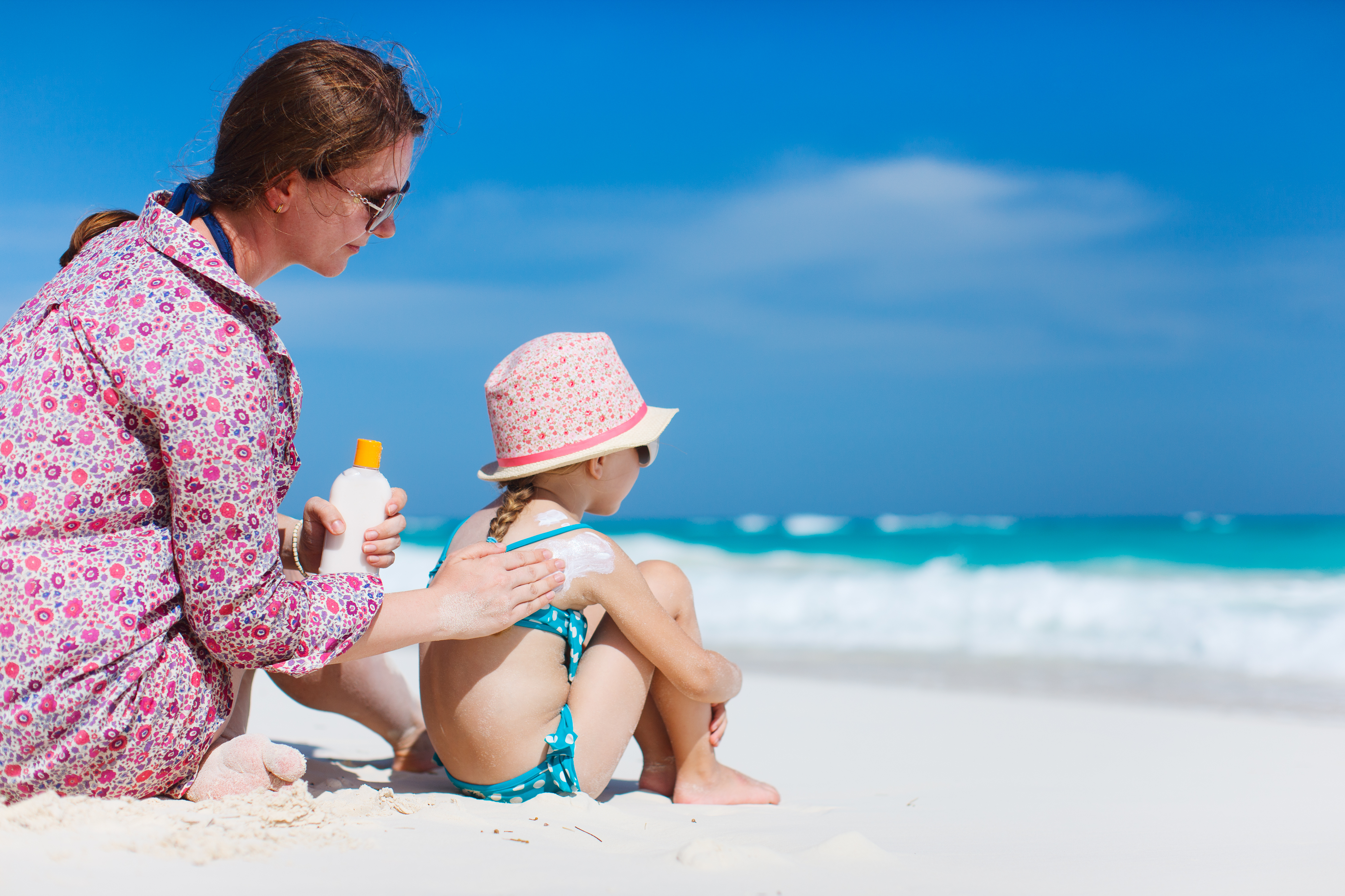 A woman rubs sunscreen on her child at the beach