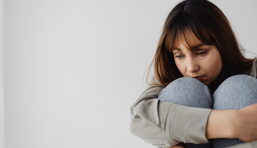 Women sitting hugging her legs looking at the ground with sad facial expression
