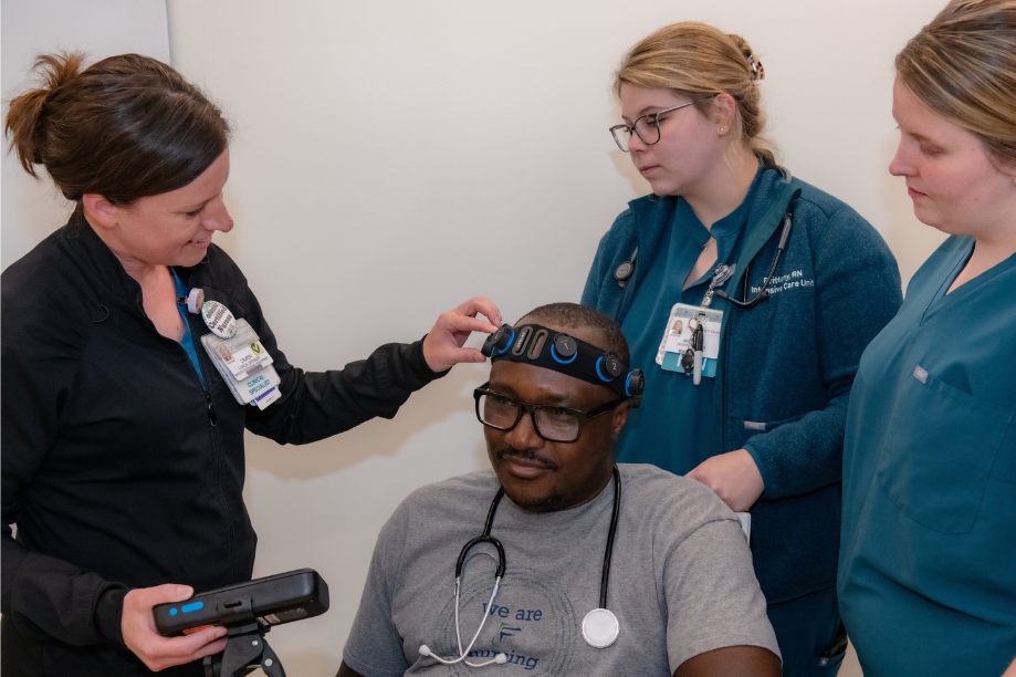 Three nurses stand around seated nurse training with headband